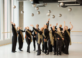Group in black and gold costumes tosses silver balls in bright dance studio