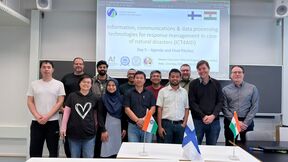 Group of students in a classroom, standing before a disaster response slide, with Finnish and Indian flags on table
