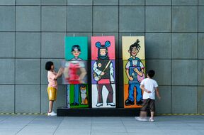 Two children play with bright cartoon panels on a grey tiled wall, spinning sections to mix the figures.
