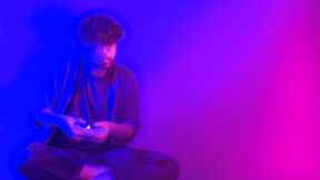 A stylized, illustrative image of a person playing a videogame, holding a game controller, surrounded by blue and magenta light.