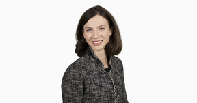 Smiling woman with straight brown hair in a grey patterned blazer, facing the camera on a white background