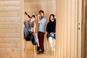 Three young people on stools in a wooden room, holding microphones and posing playfully