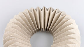 A folded origami structure with symmetrical pleats curves across a grey background.