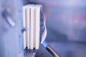 Blowtorch flame charring the side of stacked wooden boards in a metal test rig