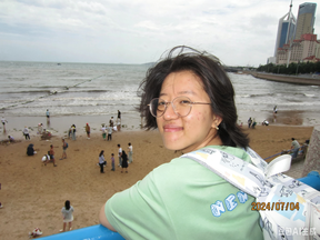 Smiling person in glasses on a seaside pier, crowded sandy beach and city skyline in the background