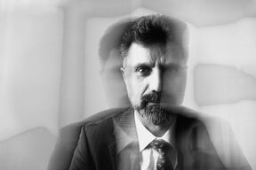 Black and white double exposure of a bearded man in a suit and tie, looking serious at the camera