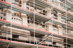 Metal scaffolding covers an ornate beige stone building with tall windows during renovation