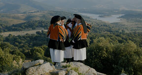 he picture shows a sunny day, in a natural landscape upon a cliff, stand four men in traditional Sardinian costumes, in the 
act of singing.