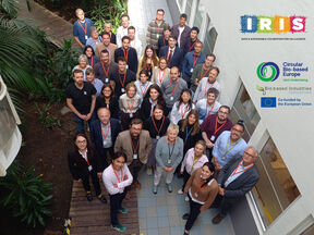 Group of conference participants with name badges, standing indoors beside plants and EU project logos