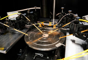 Close-up of a microchip wafer on a metal probe station with fine gold test needles around it