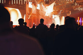 Crowd watching stage show in warm orange light, with abstract geometric structures above