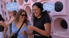 Two laughing women chat in speech bubbles outside a pink wall with round openings, text unite!