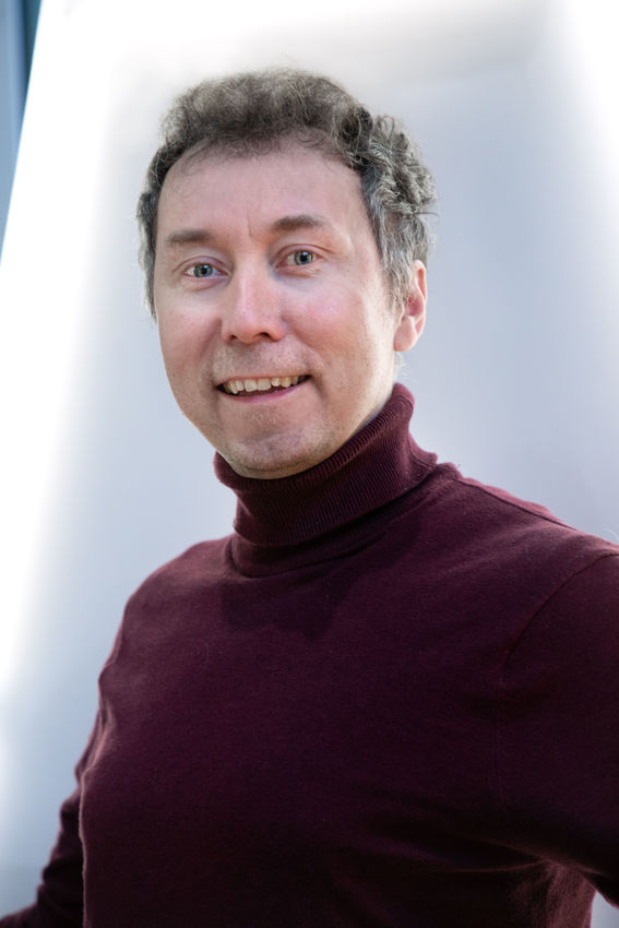 a man smiling, wearing a dark red pullover