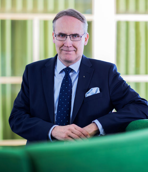 Kuvassa mies puku päällä vihreän taustan edessä