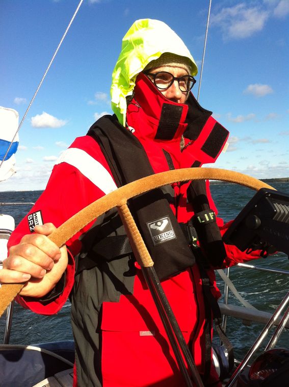 Mies seisoo purjeveneen ruorin äärellä, vaatetus kylmää vastaan jättää näkyviin vain kasvojen yläosan