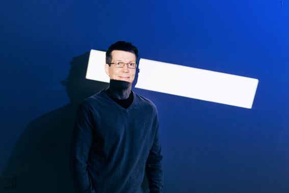 Matti Aksela kuvattuna siten, että suorakaiteen muotoinen valkoinen valo osuu hänen kasvoihinsa, tausta on tumma, sinisävyinen.