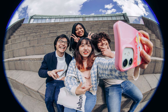 4 students taking a selfie on the steps of the Amphitheatre on Otaniemi Campus