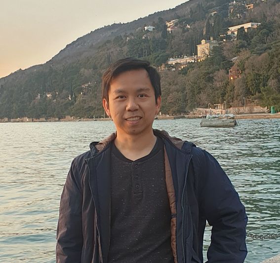 Photo of young man standing in front of hill by water