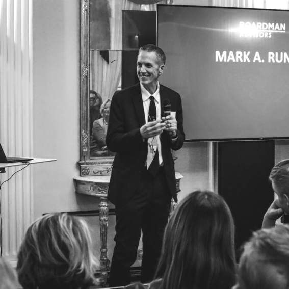 Mark Runco puvussa puhuu tapahtumassa, pitelee mikrofonia. 