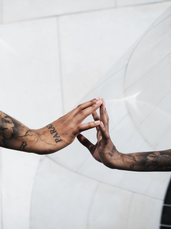 A tattooed arm with fingers touching its reflection on a glass surface, creating a mirrored effect.