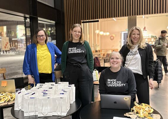 Aalto-yliopiston kesäkoulun tiimi ilmoittautumispisteellä. Neljä naista Aalto-yliopiston t-paidoissa.