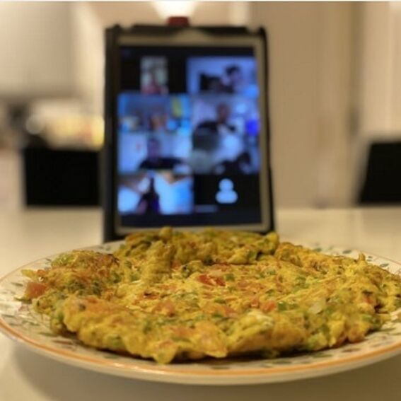 A vegetable omelette on a plate with a tablet in the background displaying a video call with multiple participants.