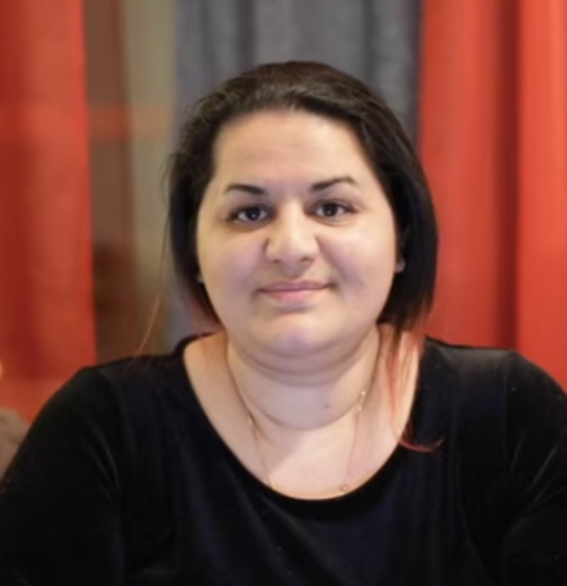 Portrait photo of young woman with dark hair in front of orange curtains