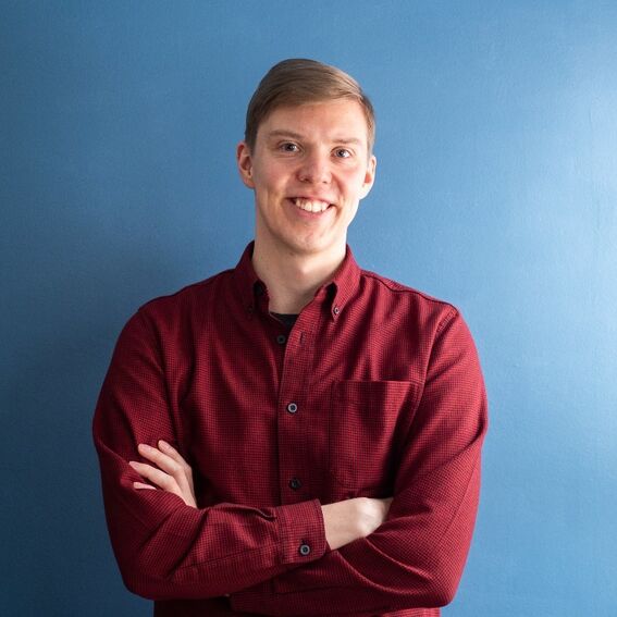 Person wearing a red button-up shirt stands with arms crossed against a blue wall.