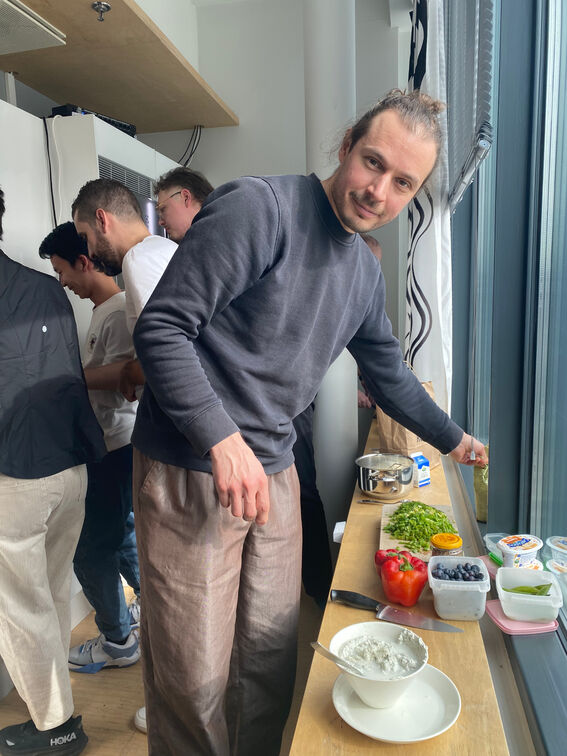 A person prepares food at a counter with various ingredients like bell peppers, chopped green herbs, and blueberries.