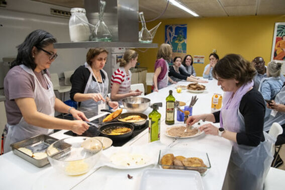 People in aprons cooking and preparing food in a kitchen together.