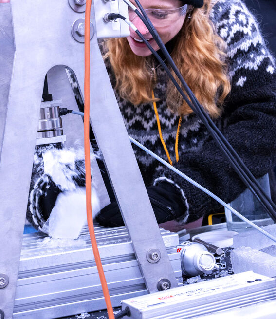 Person in winter attire operating machinery with snow or ice on a metallic surface