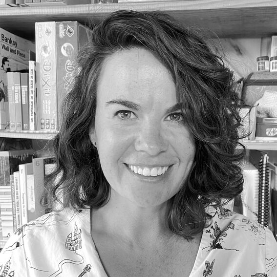 A person with curly hair is standing in front of a bookshelf filled with books and games.
