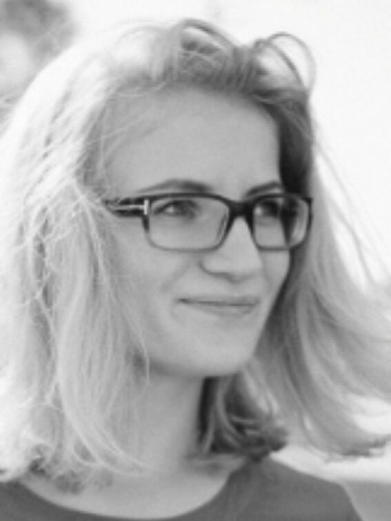 Person with short, blonde hair wearing glasses and a round-neck shirt