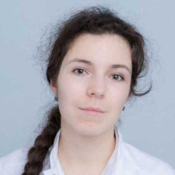 Person with long brown hair in a braid, wearing a white shirt, against a light blue background.