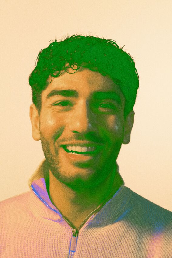 A person wearing a light-coloured zip-up sweater with a necklace, against a plain background.