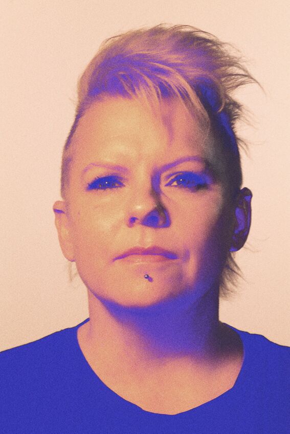 Person with spiky hair wearing a dark shirt against a light background.