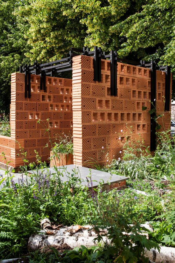 Avoin terrakottatiilipaviljonki mustine palkkeineen rehevän vihreän kasvillisuuden keskellä