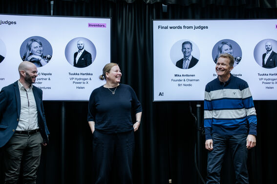 Three people stand in front of two large judge-introduction screens at an indoor event.