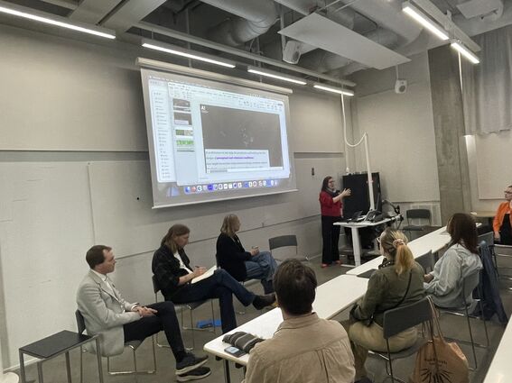 Woman presenting slides in a modern classroom while students sit in rows listening and taking notes