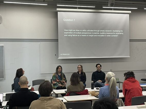 Panel of four speakers in a classroom, seated before a large projected slide titled Question 1.