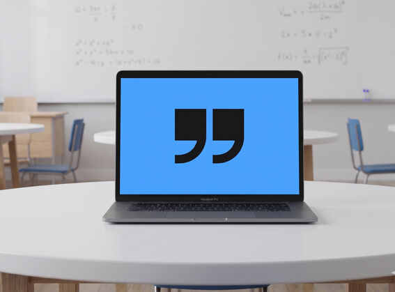 Open laptop on round table in classroom, blue screen showing large black quotation marks