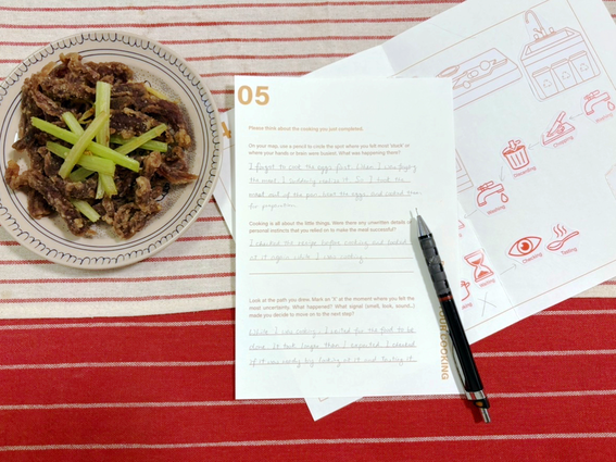 Plate of meat and celery beside handwritten cooking notes and pen on a striped red cloth