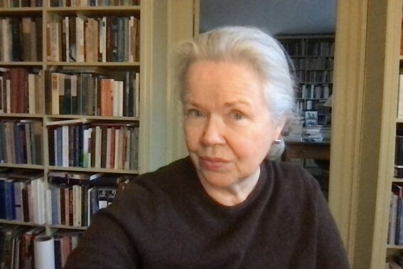 Person with grey hair in a dark top sits in a book-lined study, face blurred for privacy