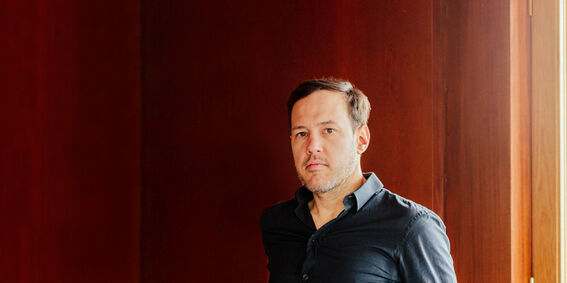Person with blurred face in dark shirt standing by a wooden wall near a bright window