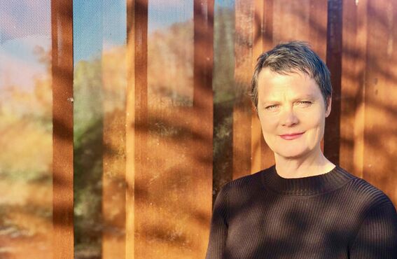 Person with blurred face in dark jumper standing by sunlit wooden wall with shadows