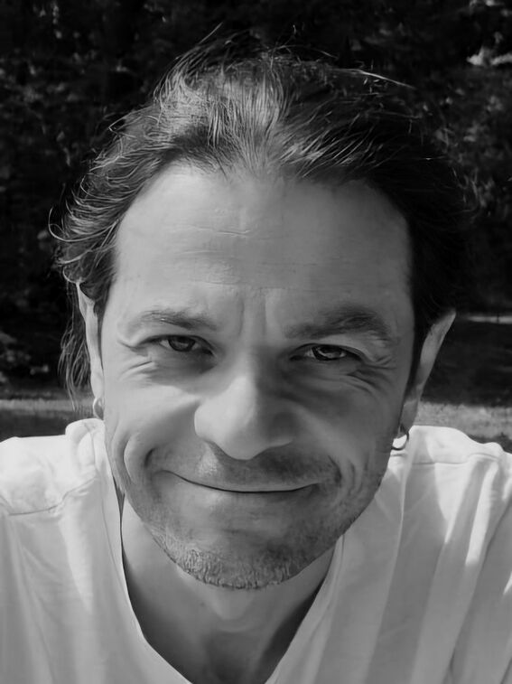 Black and white close-up of a smiling person outdoors, wearing a light shirt and small hoop earrings.