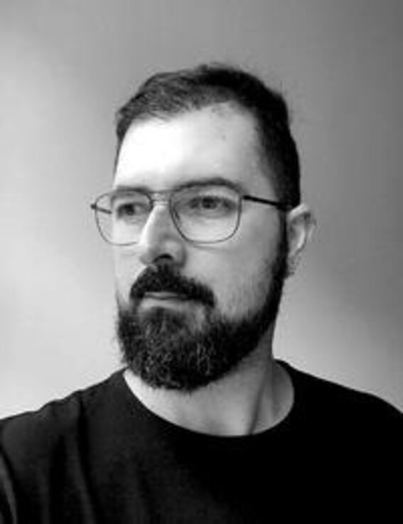 Black-and-white portrait of a bearded man with glasses in a dark shirt, looking to the side.
