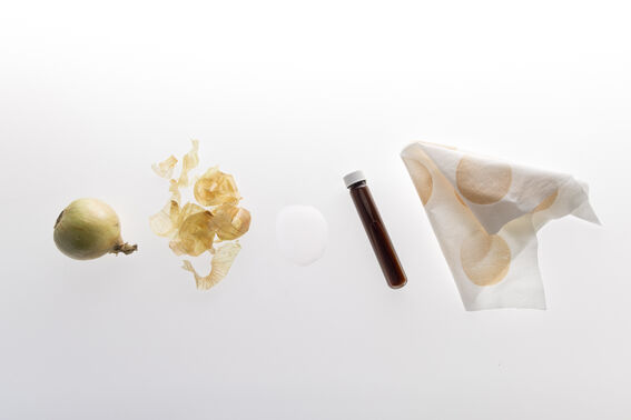 Whole onion, papery skins, brown liquid vial and patterned white cloth on plain background