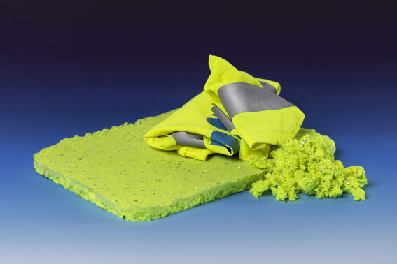 Folded hi-vis yellow fabric on a flat foam slab with loose foam pieces, on a blue gradient background