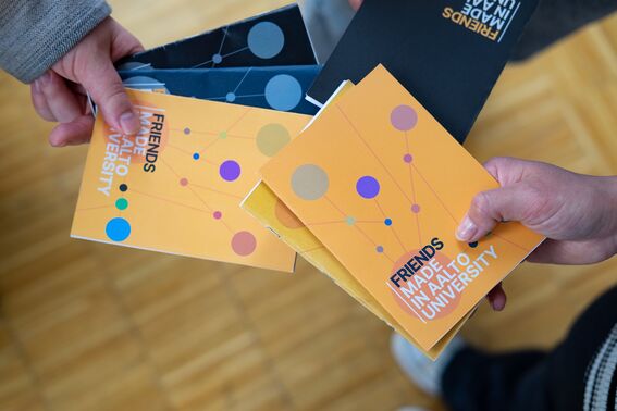 Two people hold colourful Aalto University friend book samples in their hands